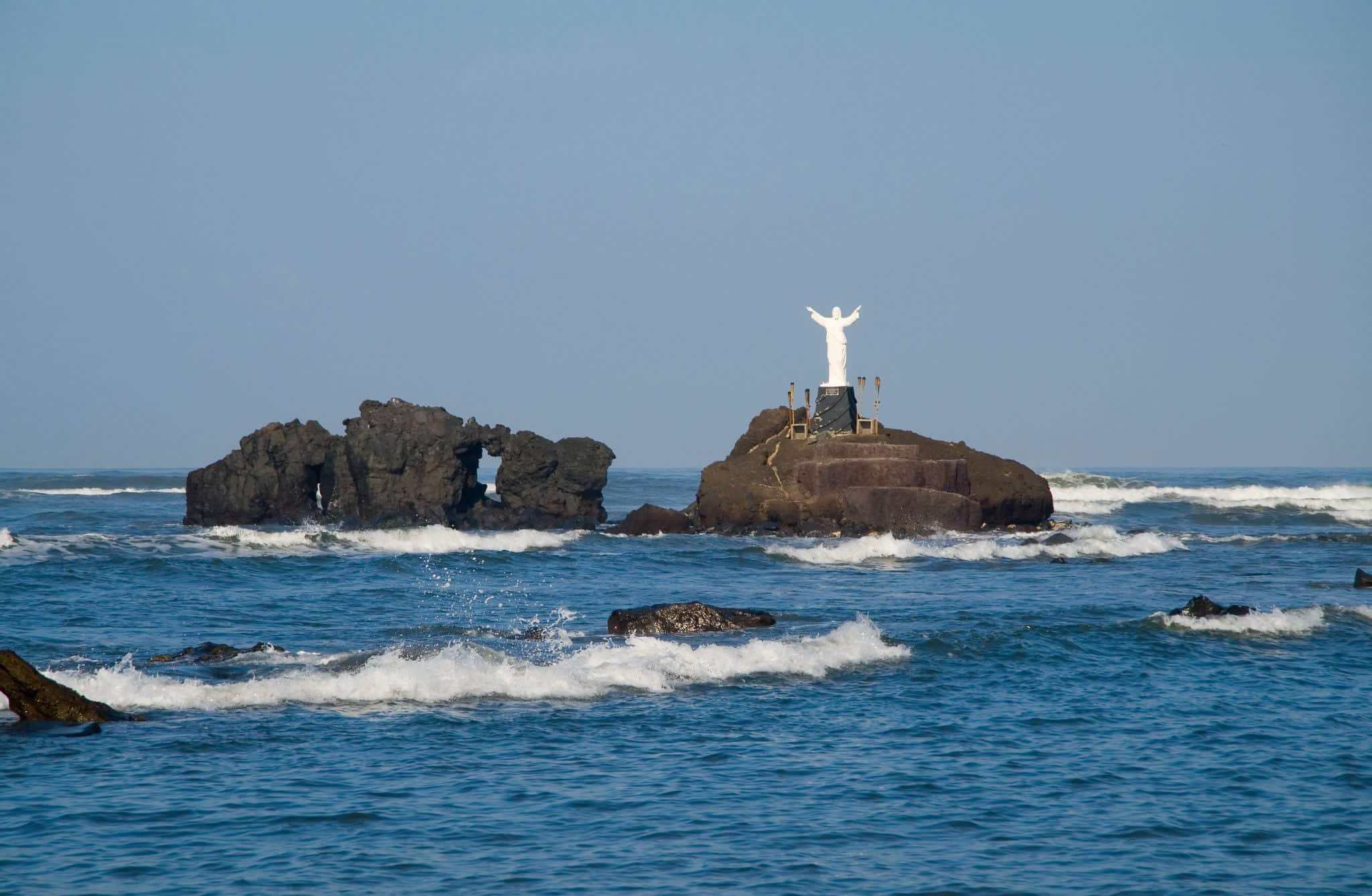 A statue of Jesus stands on a small island of volcanic rocks