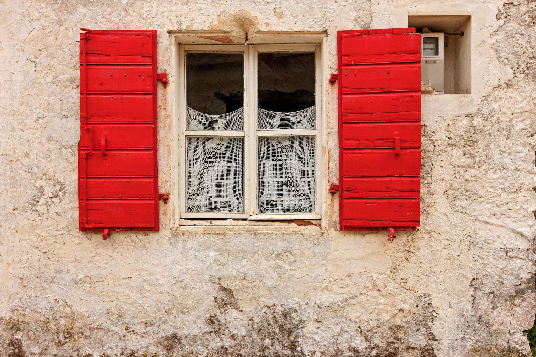 Picturesque facade of traditional local house with stone wall, red window and elaborate lace as curtains, seen in a village of Zakynthos island, Ionian Sea, Greece, Europe.
