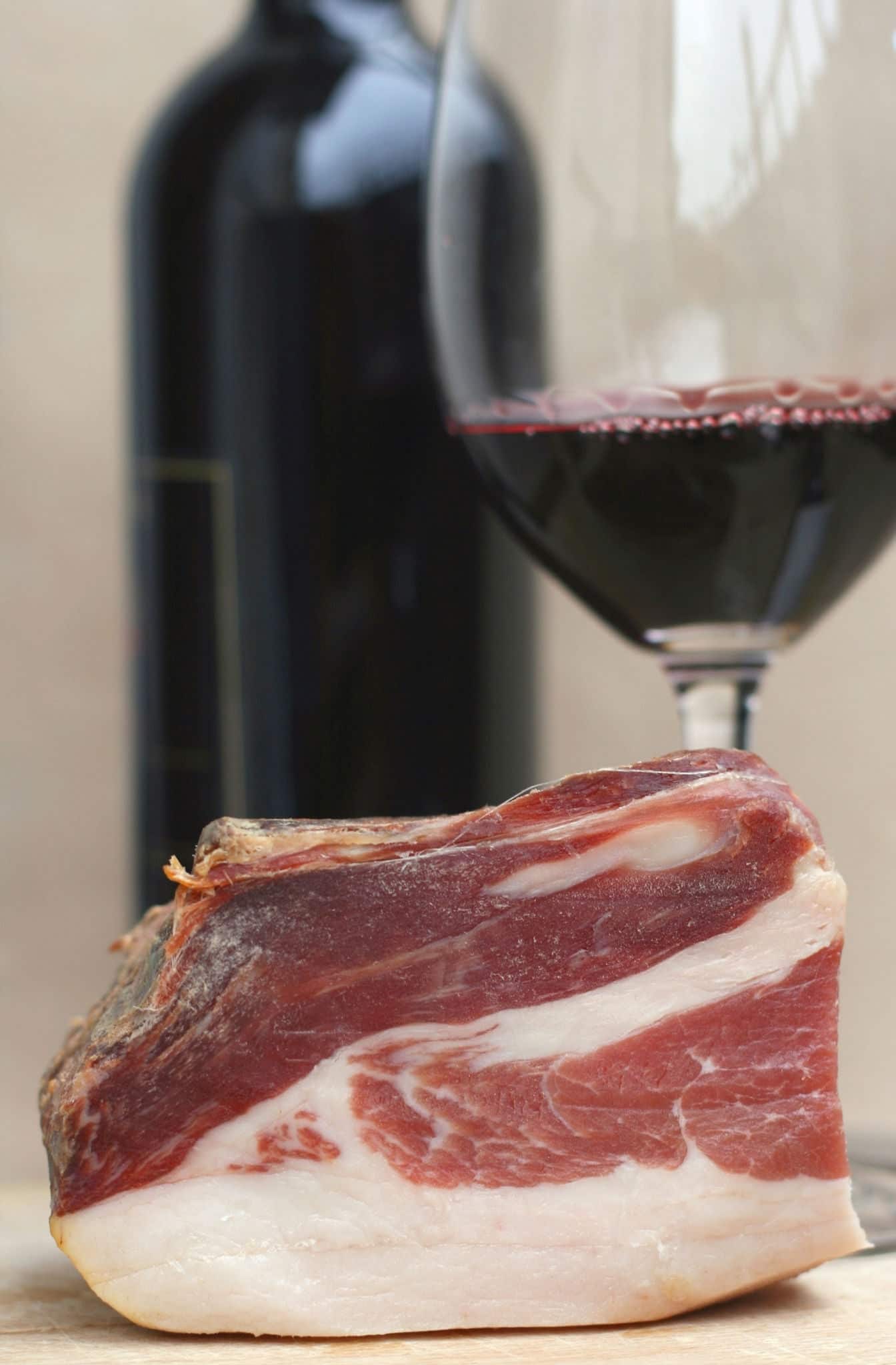 Typical Slovenian dry cured smoked ham called prsut from Slovenia with red wine in background