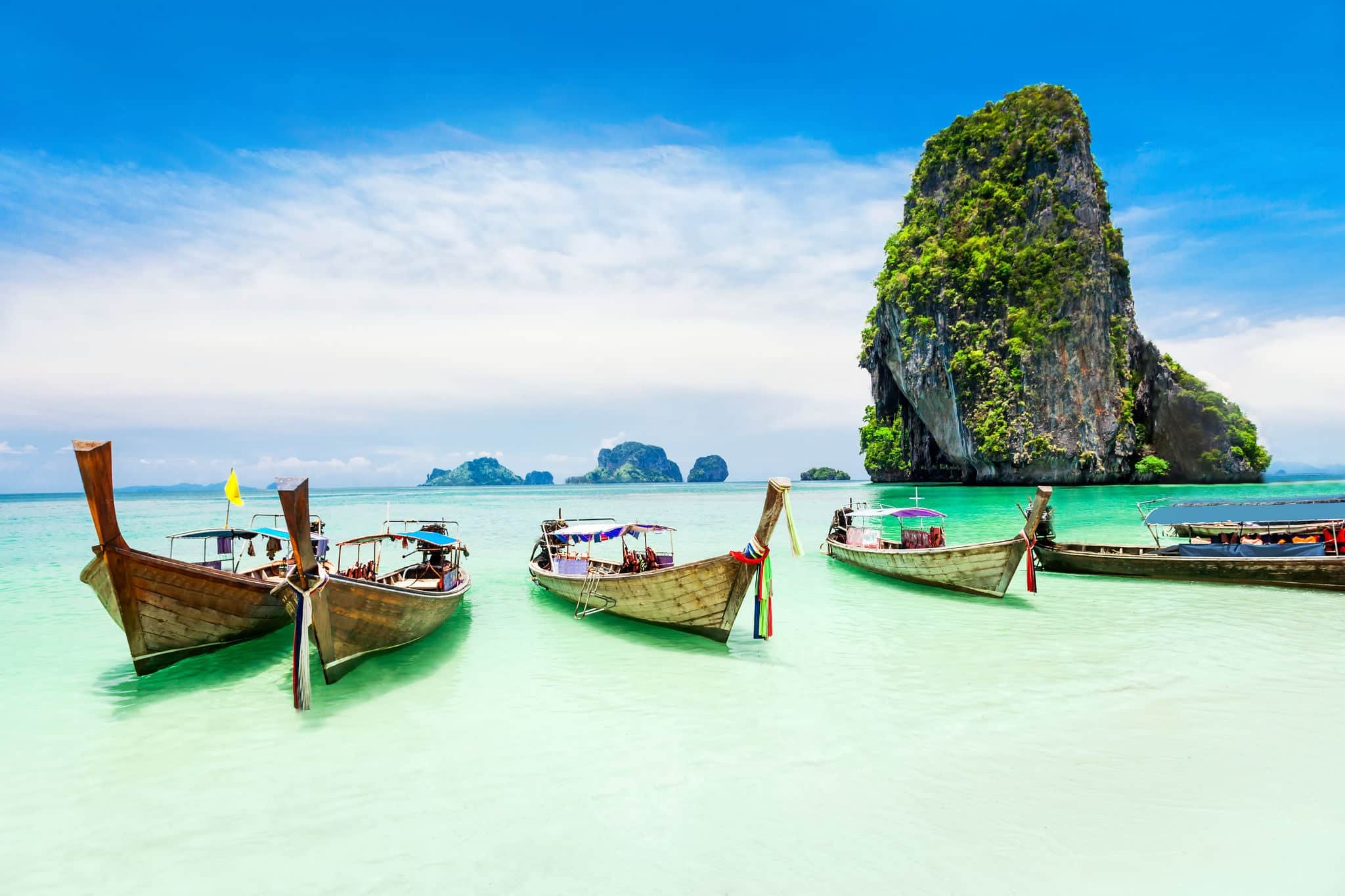 Longtale boats at the Phuket beach with limestone rock on background in Thailand. Phuket island is a most popular tourist destination in Thailand.