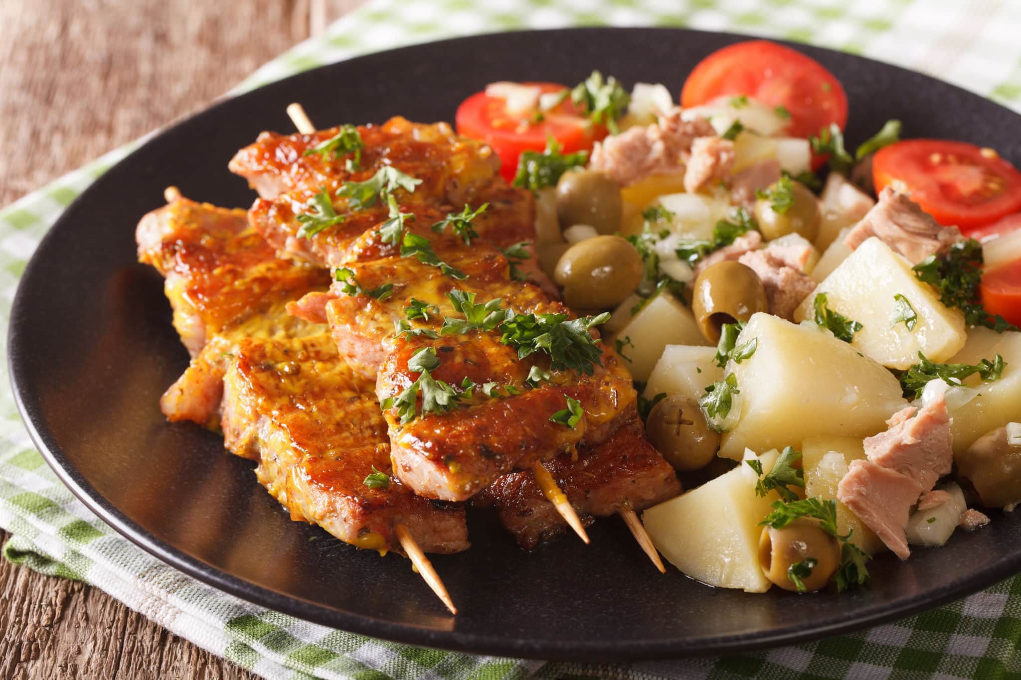 Spanish skewers Pinchos Morunos and potato salad with tuna on the plate closeup. horizontal