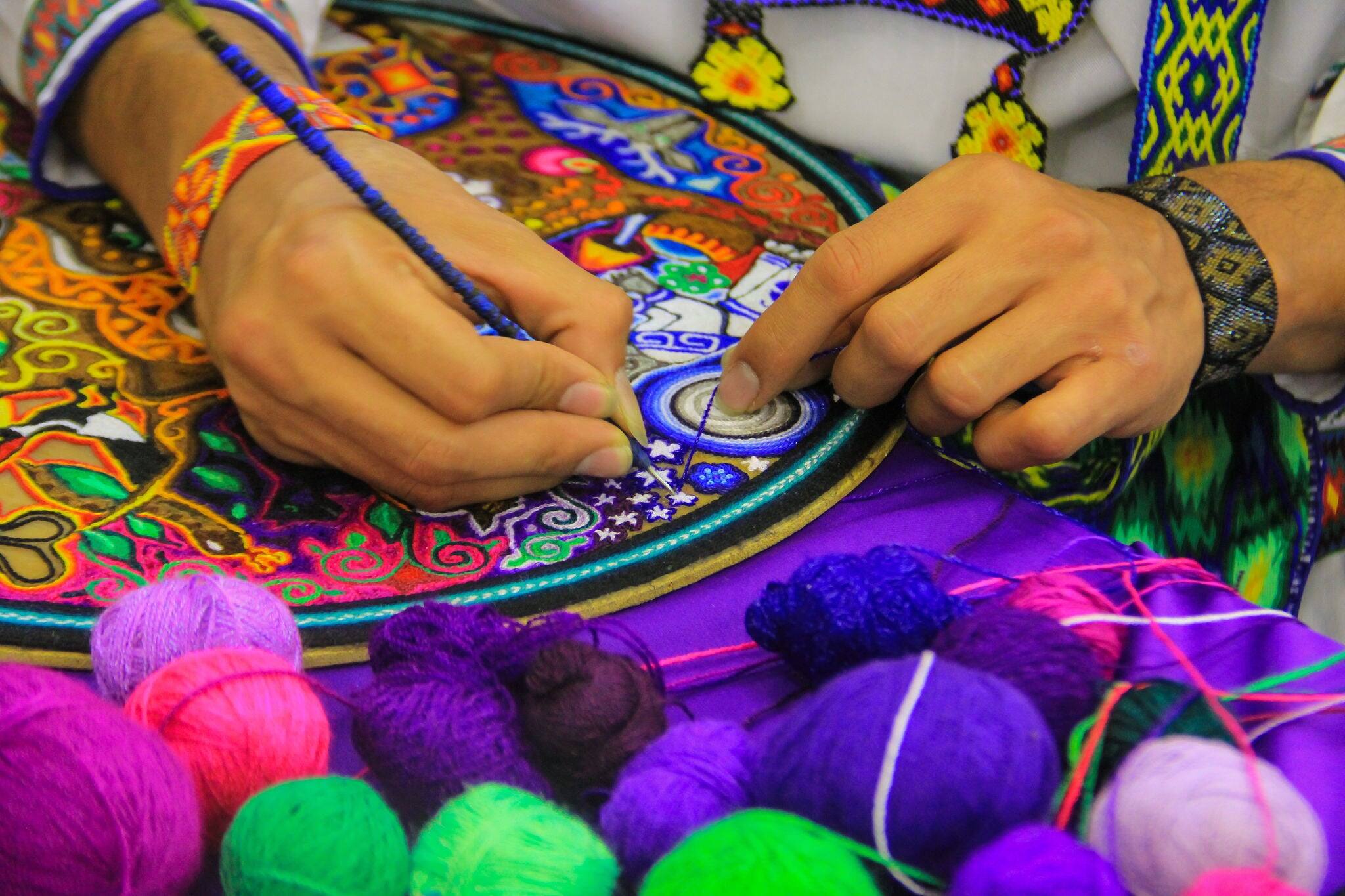 Close up of a Mexican man working of his handcraft with bokeh of yarn in front.