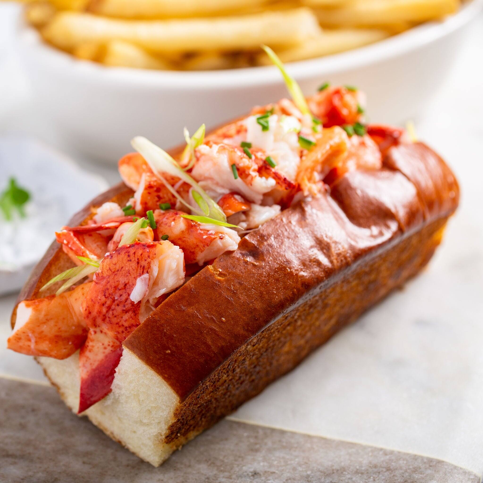 Lobster roll on a brioche bun with fries on a marble board