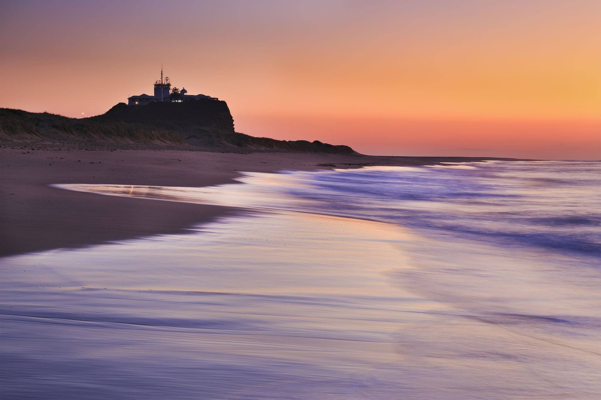 Nobbys lighthouse in Newcastle of Australia at sunrise sinking in warm pink rays of rising sun