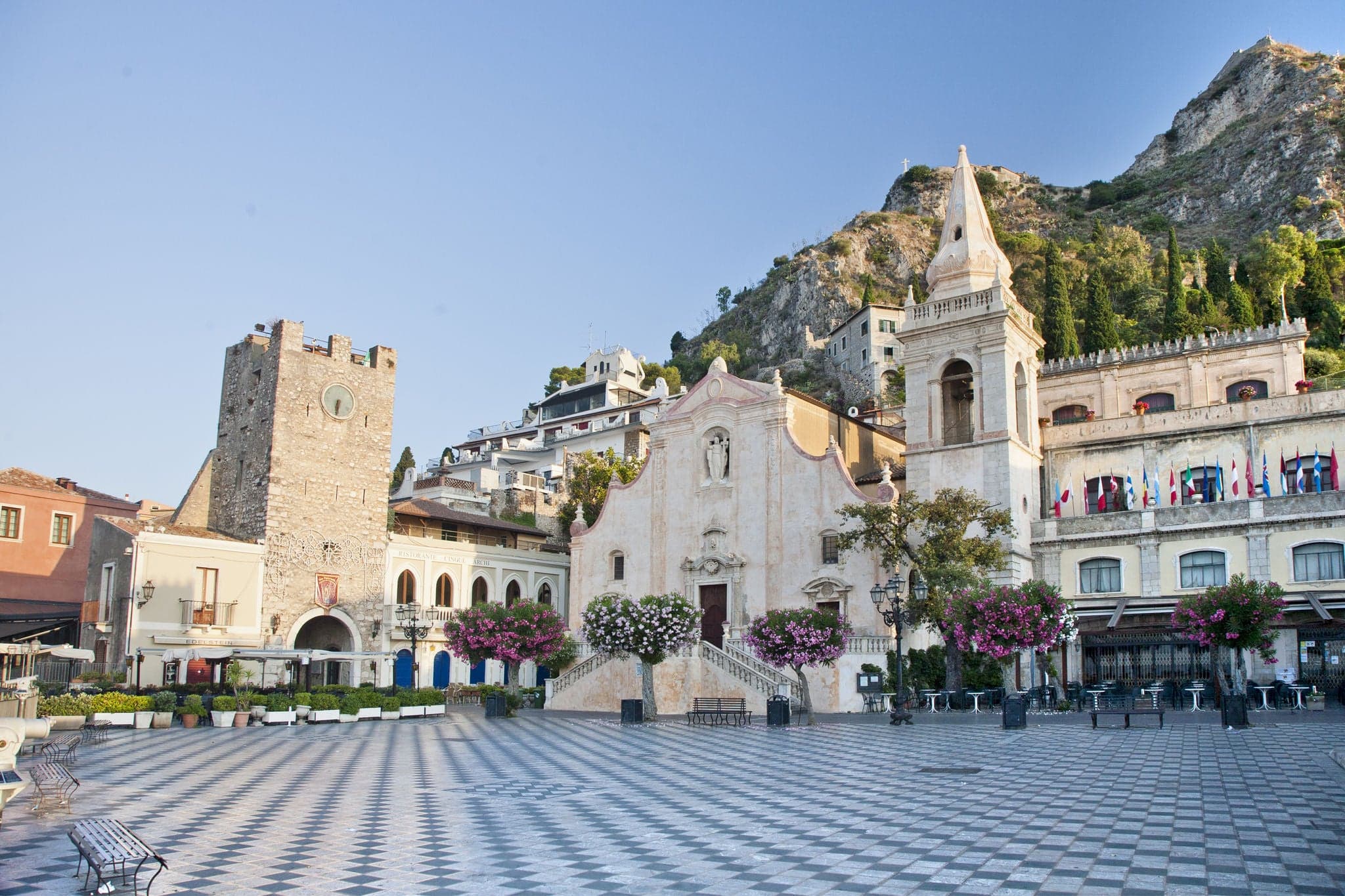 Morning panoramic view of Taormina main square (Piazza IX Aprile) with San Giuseppe Church, the Clock Tower and Mount Etna Volcano on background - Taormina, Sicily, Italy
