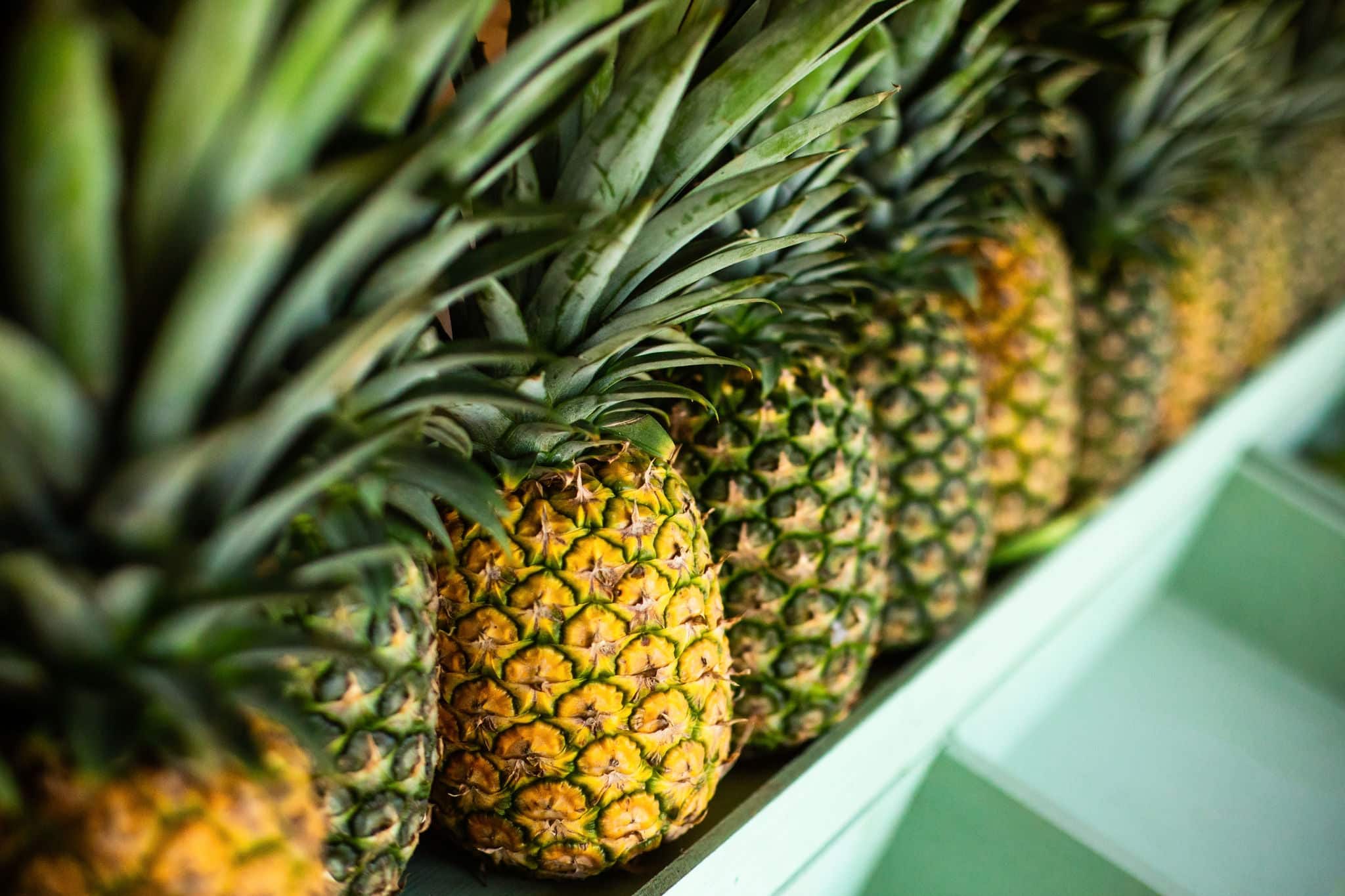 Close up of perspective view juicy ripe pineapples in a row on the wooden counter of a fruit shop on island. Colorful tropical background.
