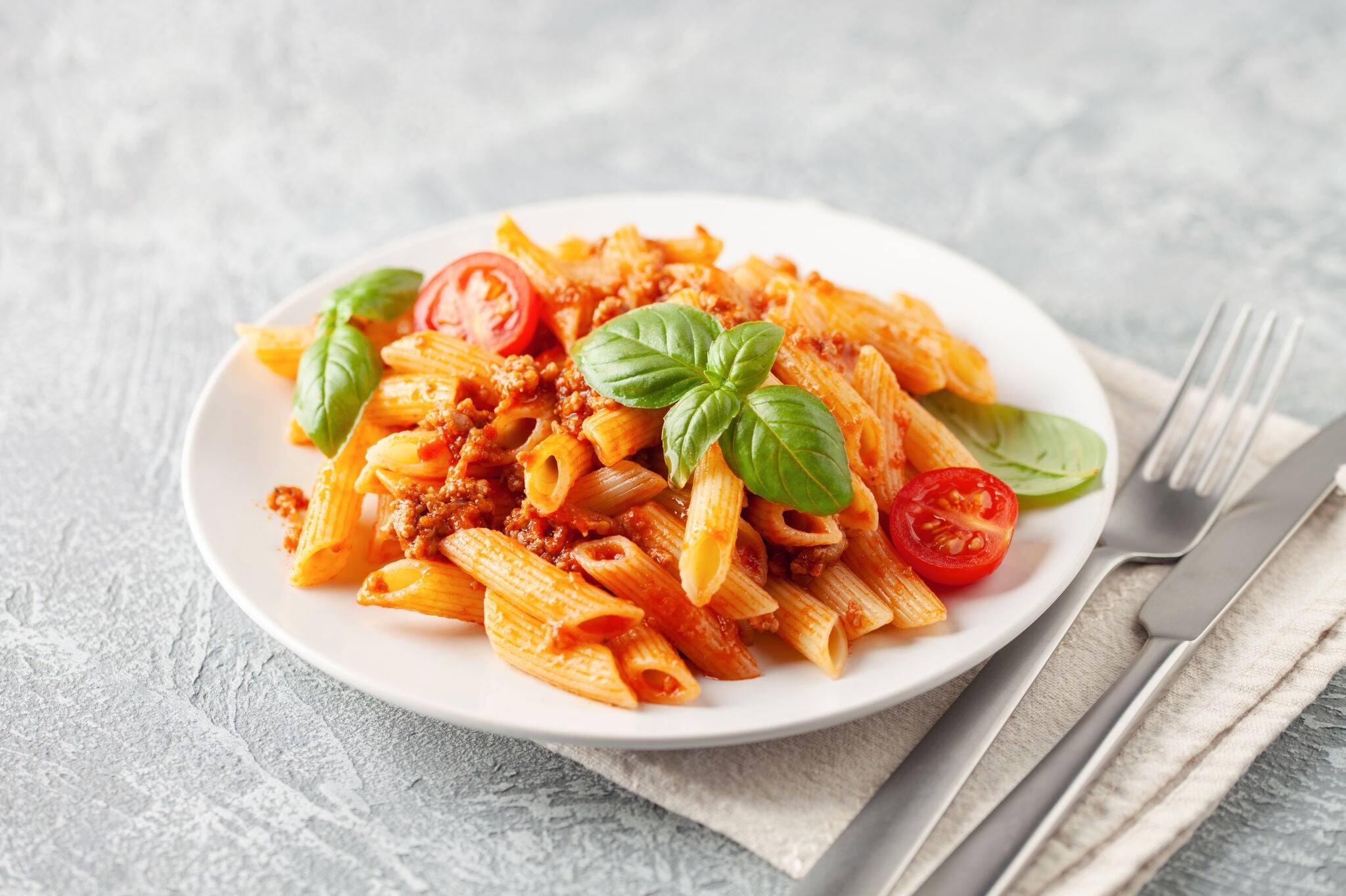 Pasta Penne Bolognese in white plate on light background. Bolognese sauce is classic italian cuisine dish. Popular italian food.