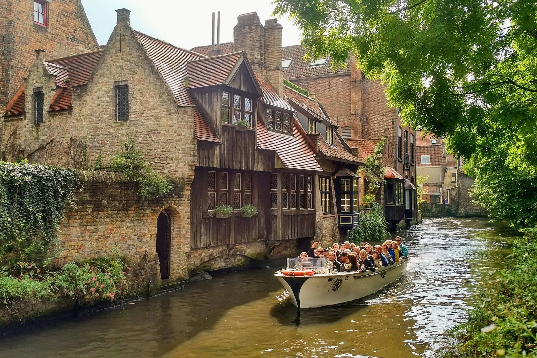 Brugges, Belgium - September 9, 2017: Tourists take a scenic boat tour to admire the beautiful medieval buildings along the canals of Brugges, Belgium.