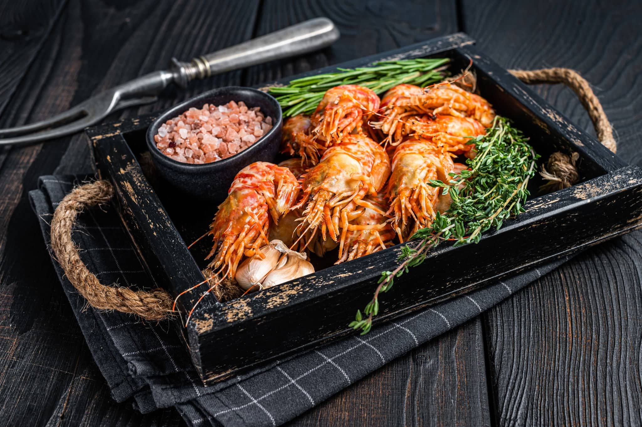 Boiled Greenland Prawn Shrimp in a wooden tray with herbs. Black wooden background. Top view