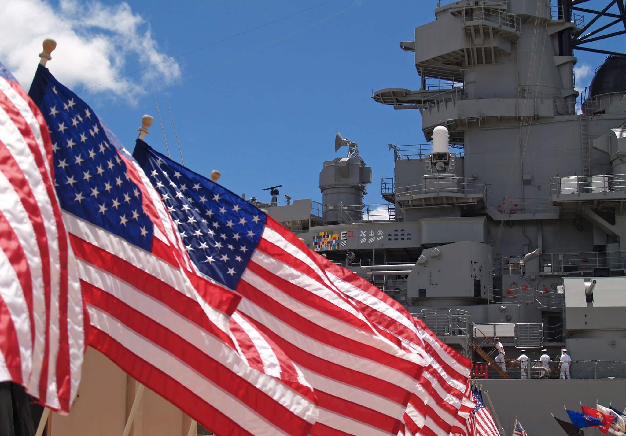 US flags flying beside the Battleship Missouri in Pearl Harbor, Honolulu, Oahu, Hawaii with 4 sailors walking on deck.