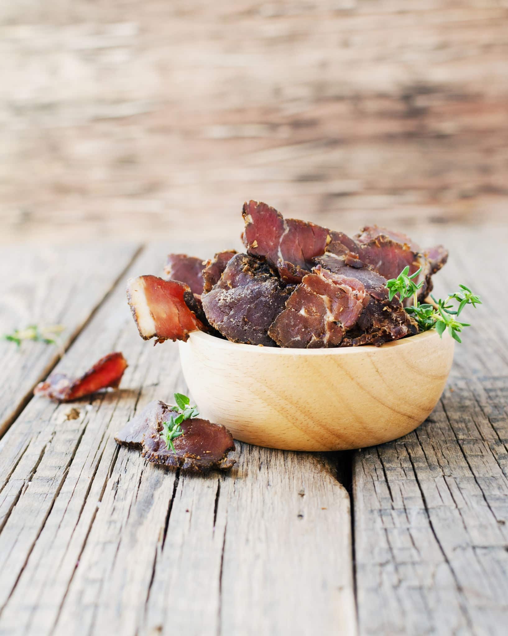 jerked dried meat, cow, deer, wild beast or biltong in wooden bowls on a rustic table, selective focus