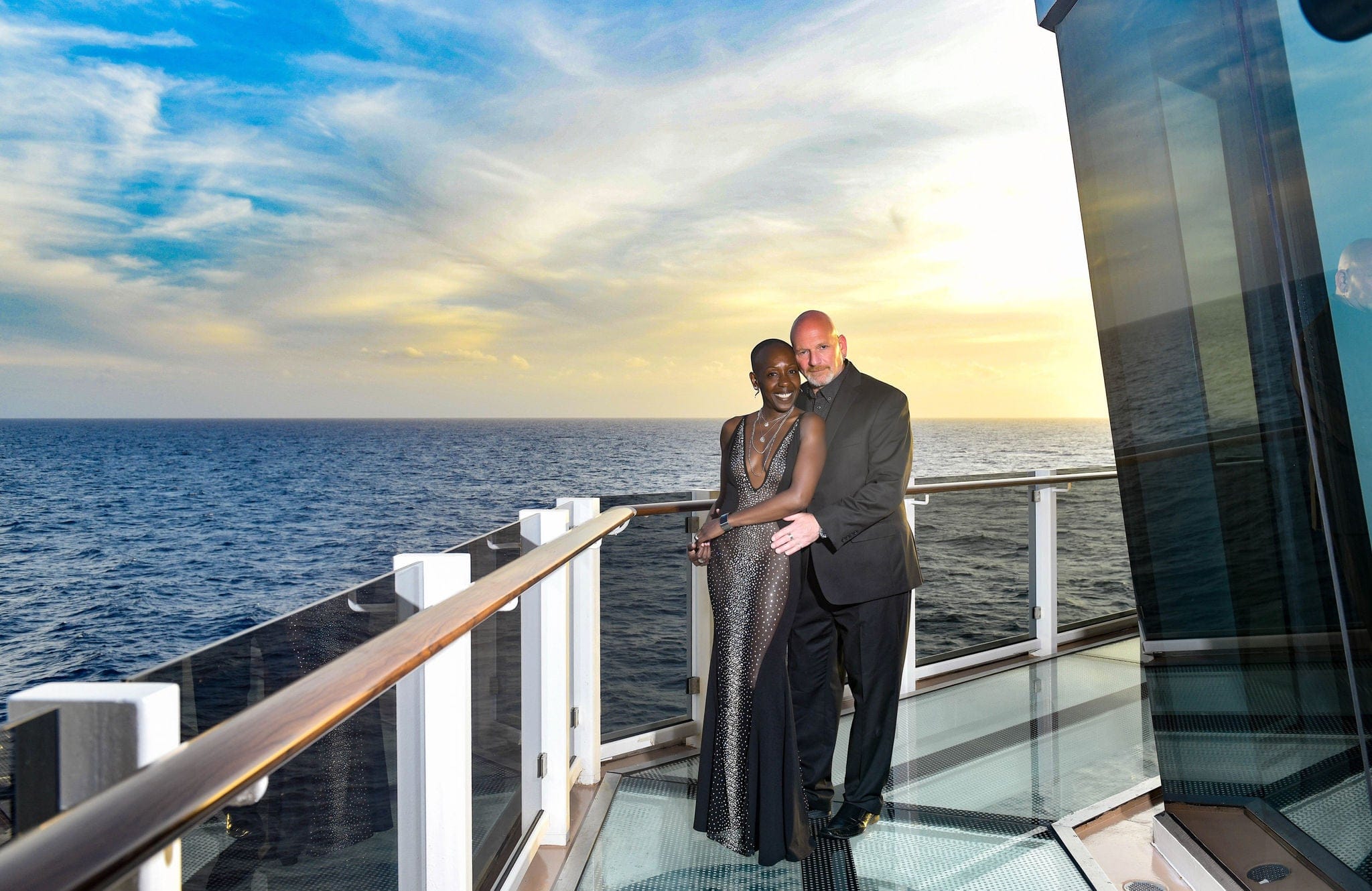 Couple in evening dress being photographed against the railing and sea behind them.