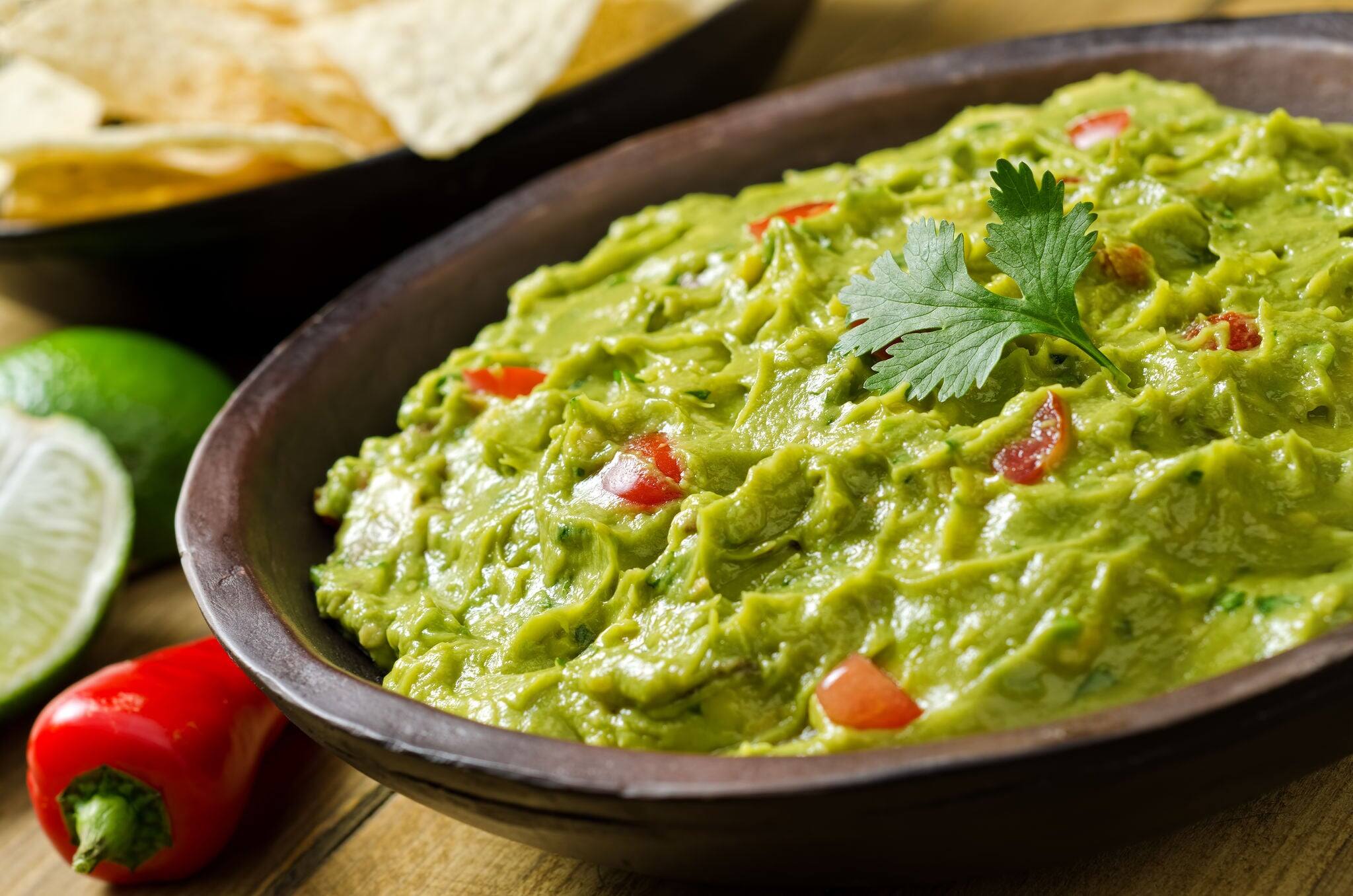 Guacamole with avocado, lime, tomato, and cilantro with tortilla chips.