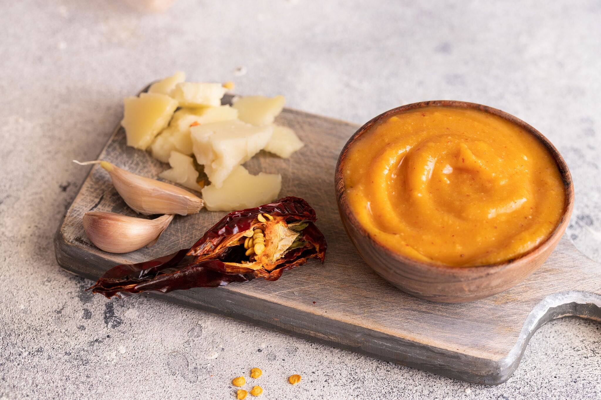 Almogrote , cheese paste form La Gomera, Canary Islands in wooden bowl on cut board with hard goat cheese, peppers  and garlic.Close up