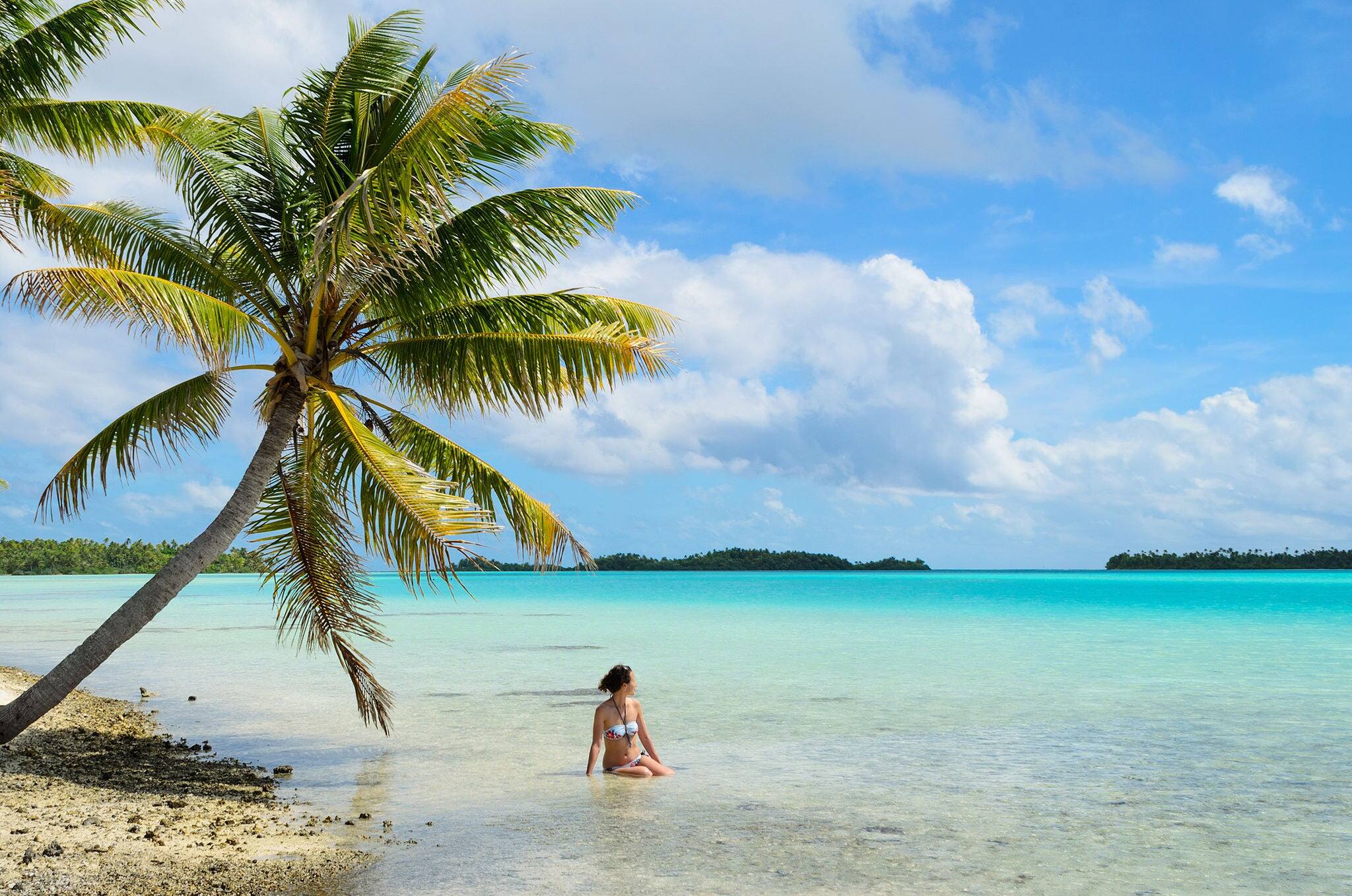 Female tourist bathing in the shallow water of the sea under a hanging palm tree on a beach on a desert island in the lagoon of Rangiroa, a tropical atoll near Bora Bora in pacific  French Polynesia.