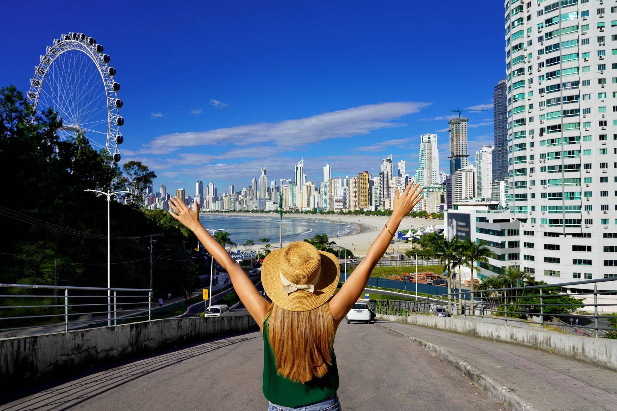 Girl with raised arms on Balneario Camboriu skyline with Ferris Wheel, Santa Catarina, Brazil
