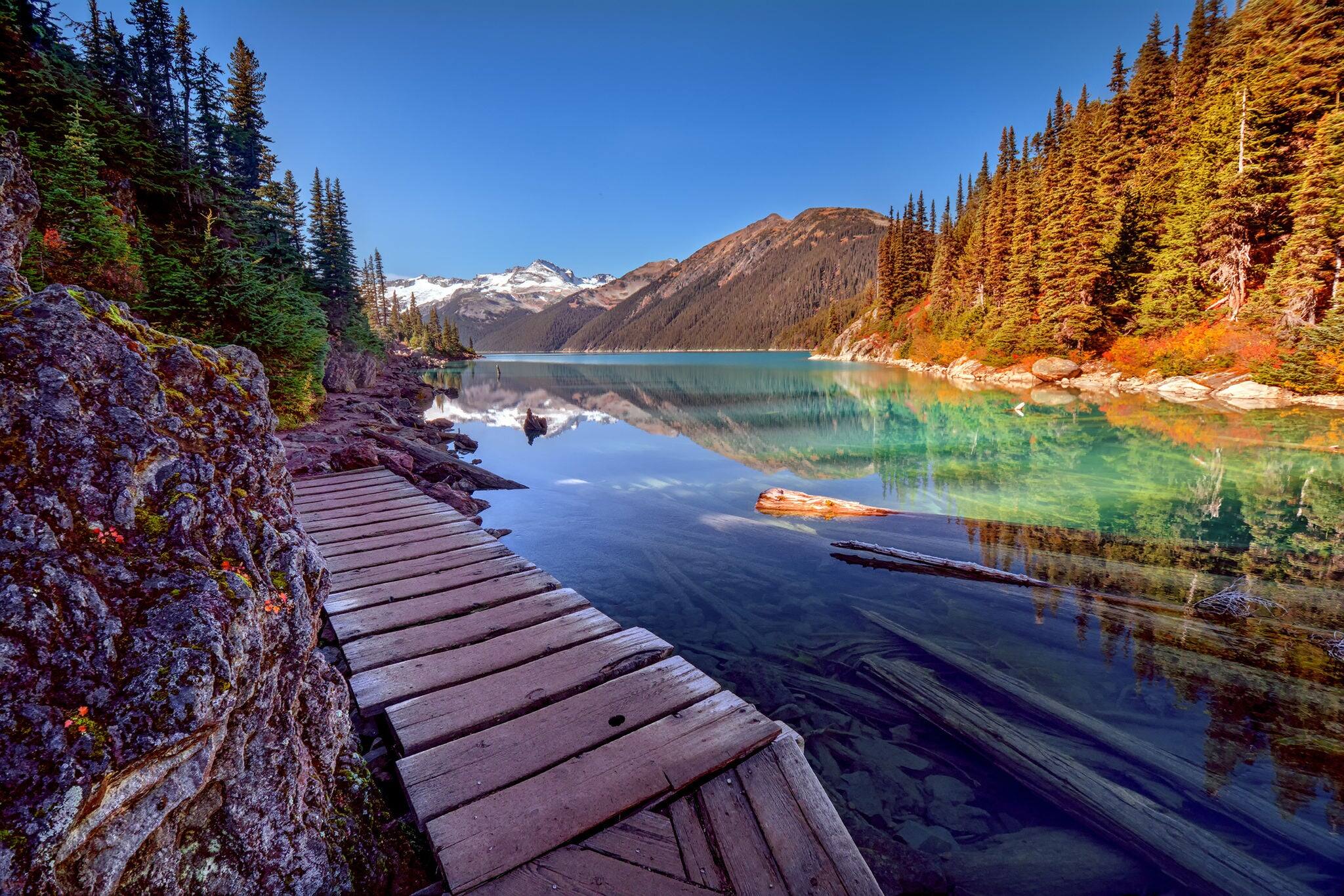 Wooden walkway along the glacial lake, with pine trees and mountains
