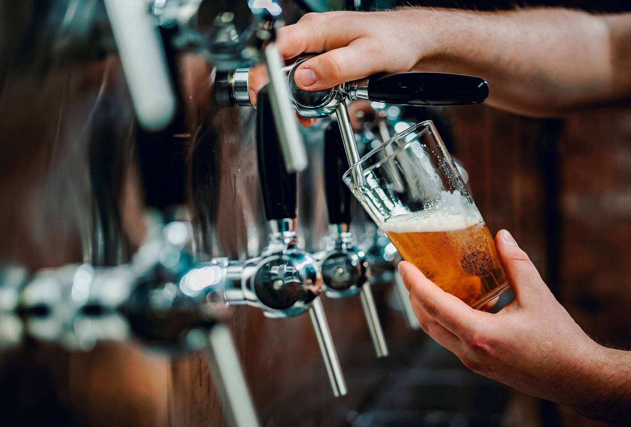 bartender hand at beer tap pouring a draught beer in glass serving in a bar or pub. taproom