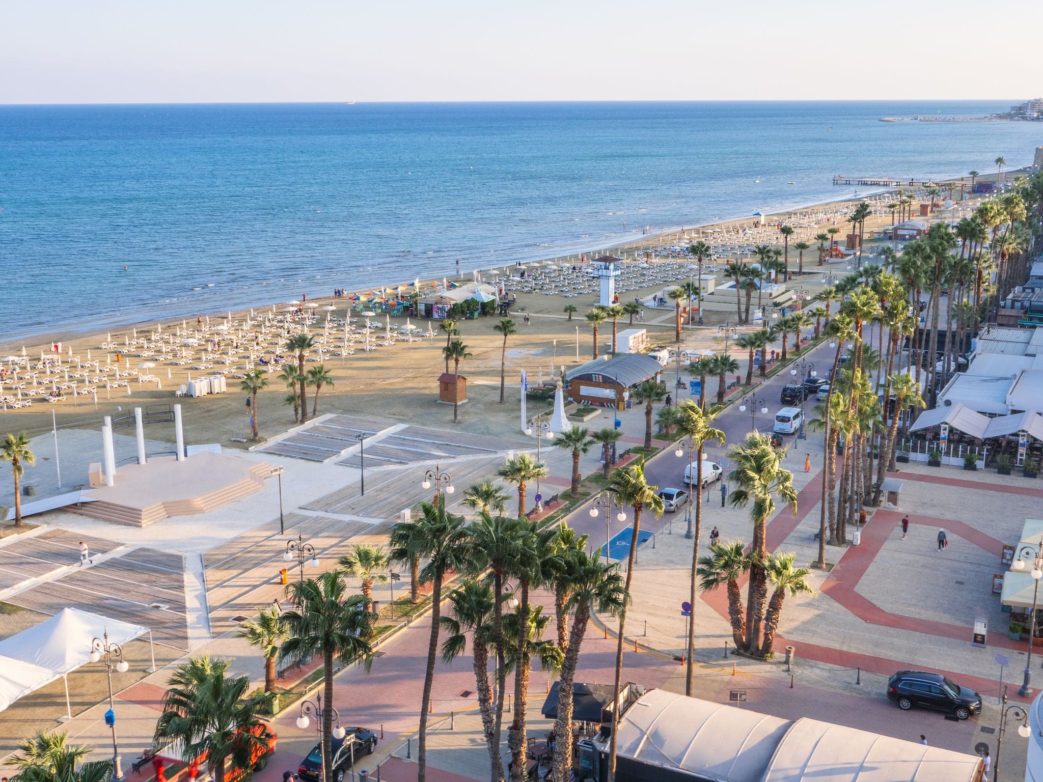Top aerial view overlooking Finikoudes Palm tree promenade, road with cars and central beach near the Mediterranean sea in Larnaca city, Cyprus.