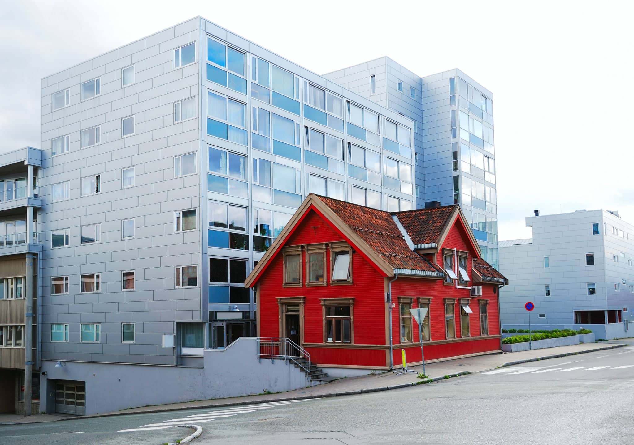 Red wooden house stands on the empty street of Tromso. Relics of the past is surrounded with modern multistory buildings.