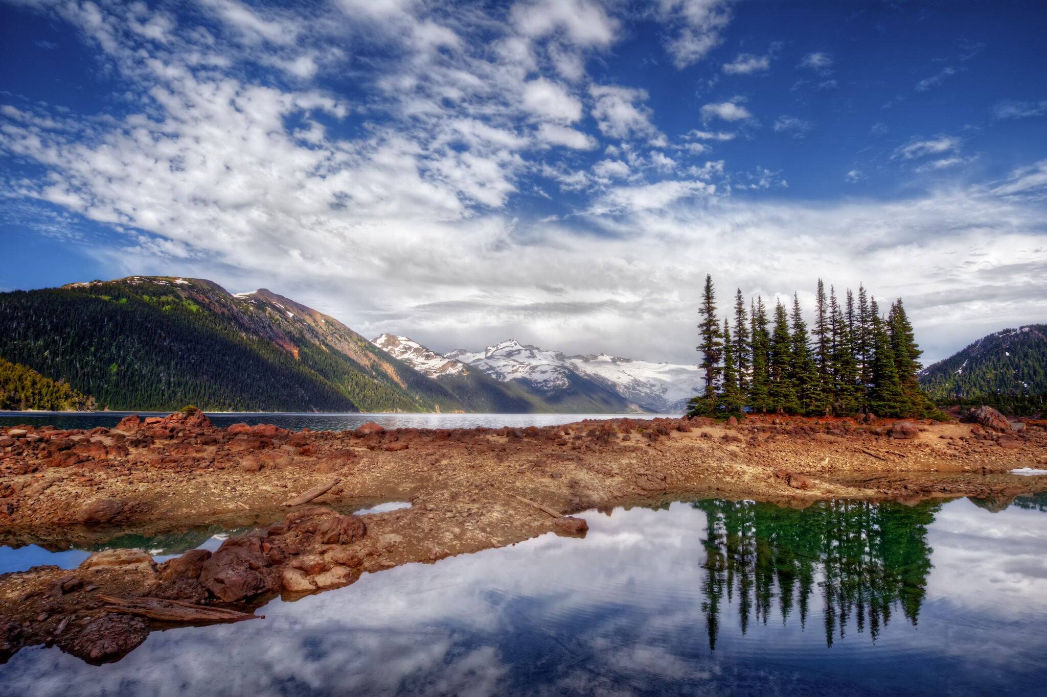 Glacial mountain lake with red blooming flowers, blue sky and dark cliffs