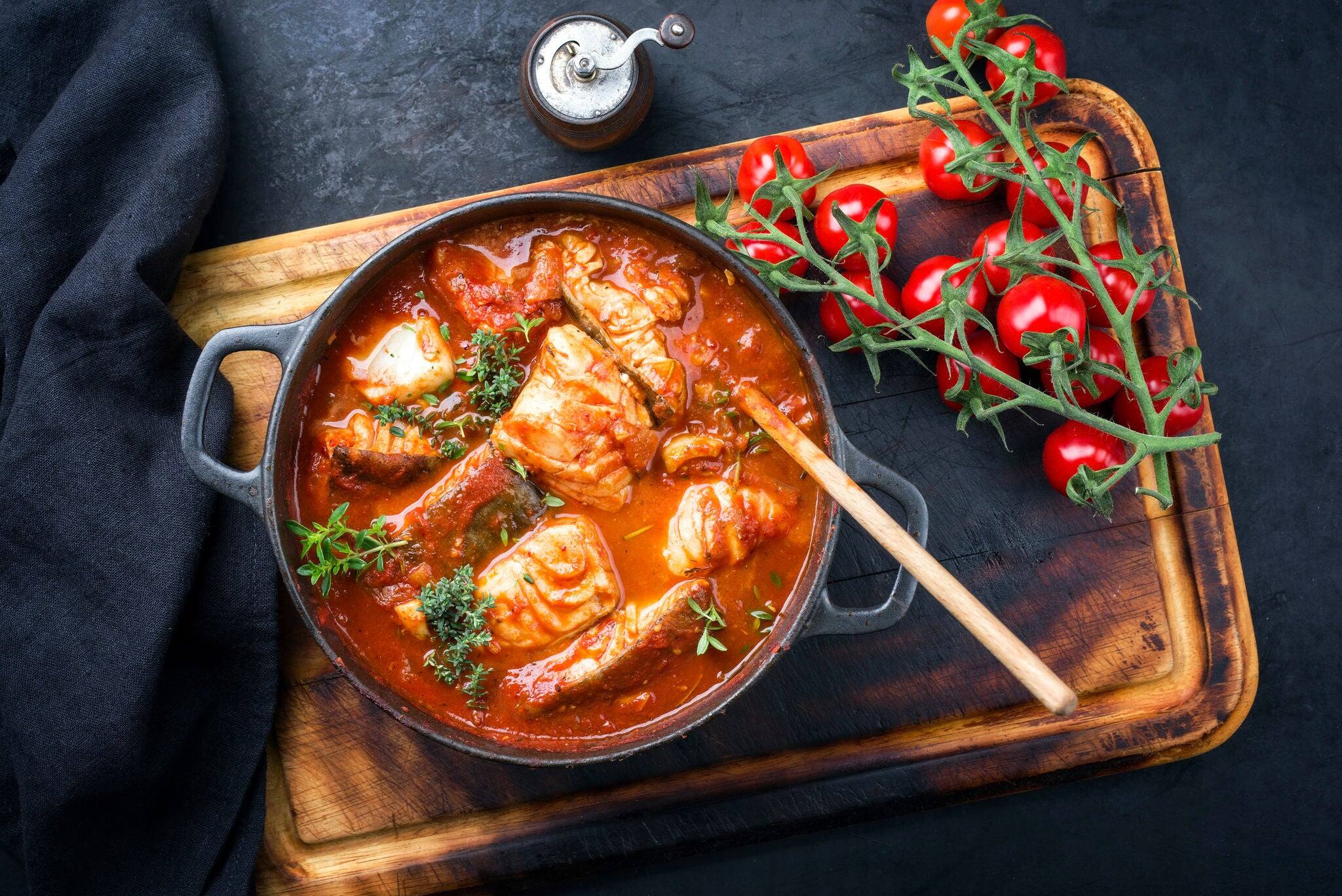 Traditional Brazilian fish stew moqueca baiana with fish filet in tomato sauce as top view in a modern design cast-iron roasting dish
