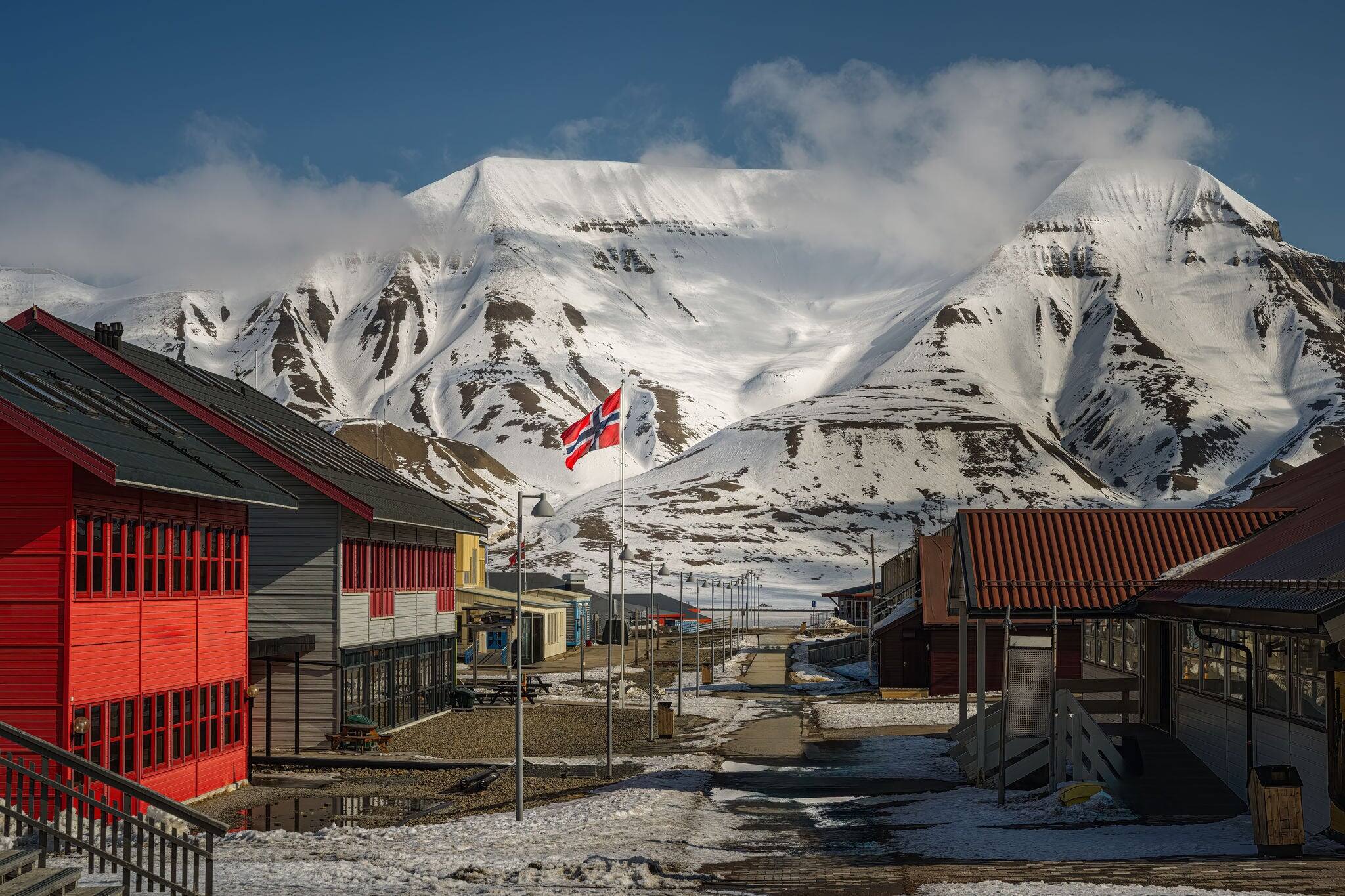 A EMPTY LONGYEARBYEN STREET ON NORWAYS INDEPENDENCE DAY WITH BRIGHT COLORED SHOPS AND A SNOW COVERED MOUNTAIN IN THE BACKGROUND WITH A NICE SKY ON SVALBARD NORWAY IN THE ARCTIC