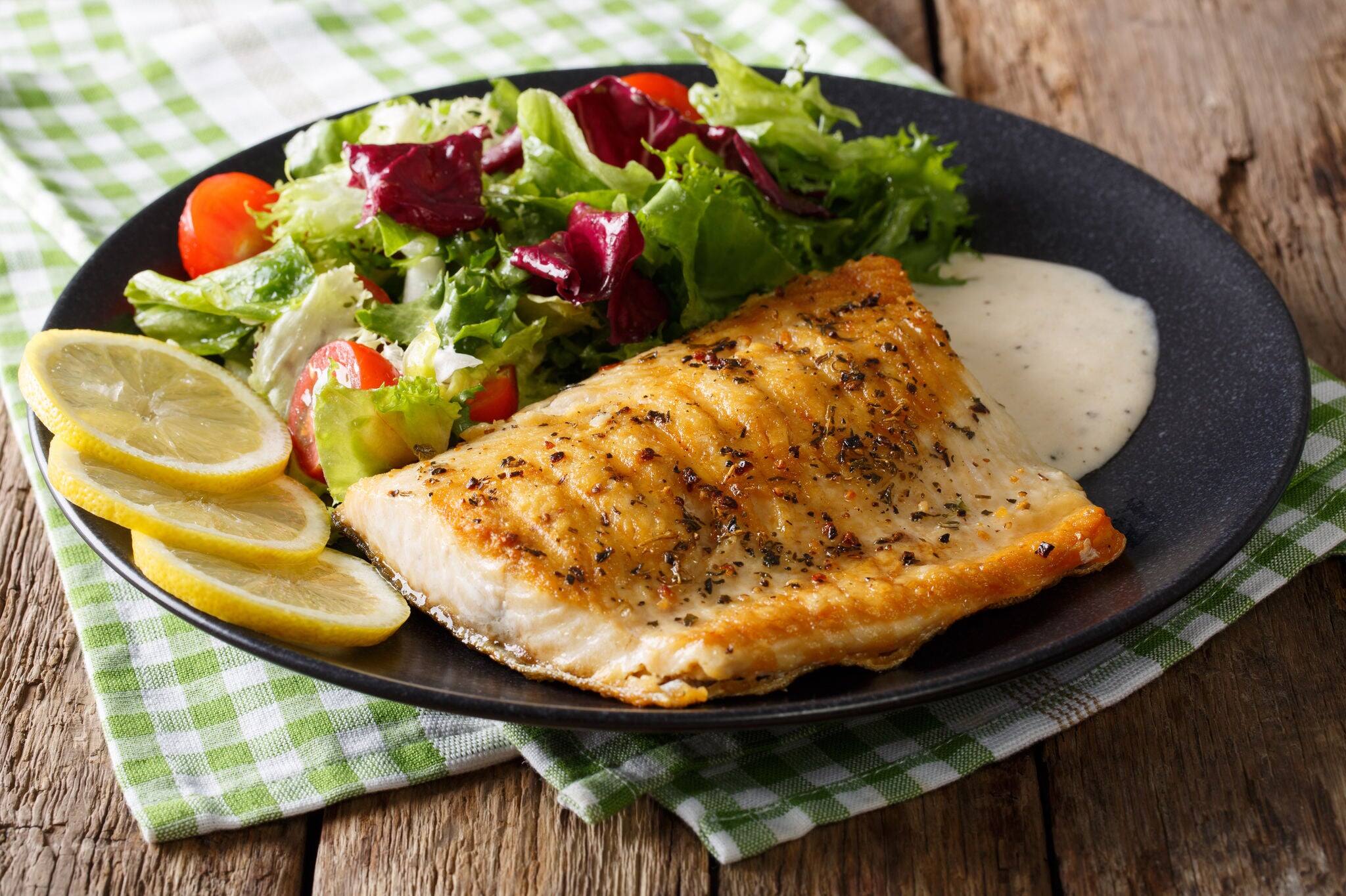 Grilled Arctic char fillet with mixed salad and sauce on a plate close-up. horizontal
