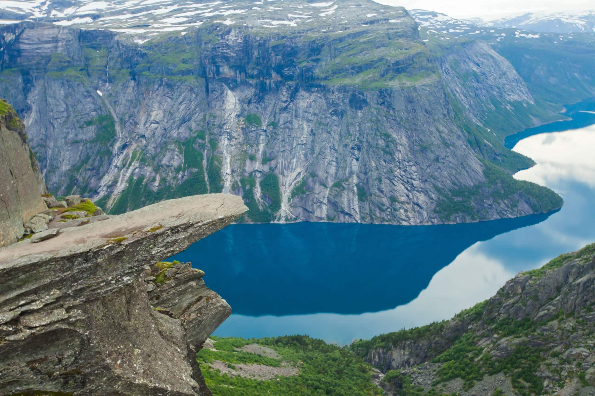 A vibrant picture of famous norwegian hiking place - trolltunga, the trolls tongue, rock skjegedall, with a tourist, and lake ringedalsvatnet and mountain panoramic scenery epic view, Norway