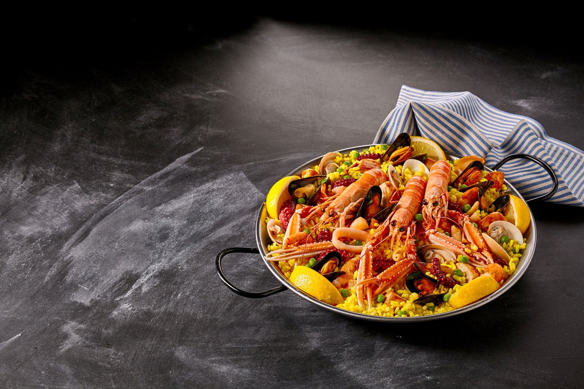 Gourmet traditional Valencia Spanish seafood paella with langoustines, mussels and clams on a bed of seasoned saffron rice on a slate background with copy space