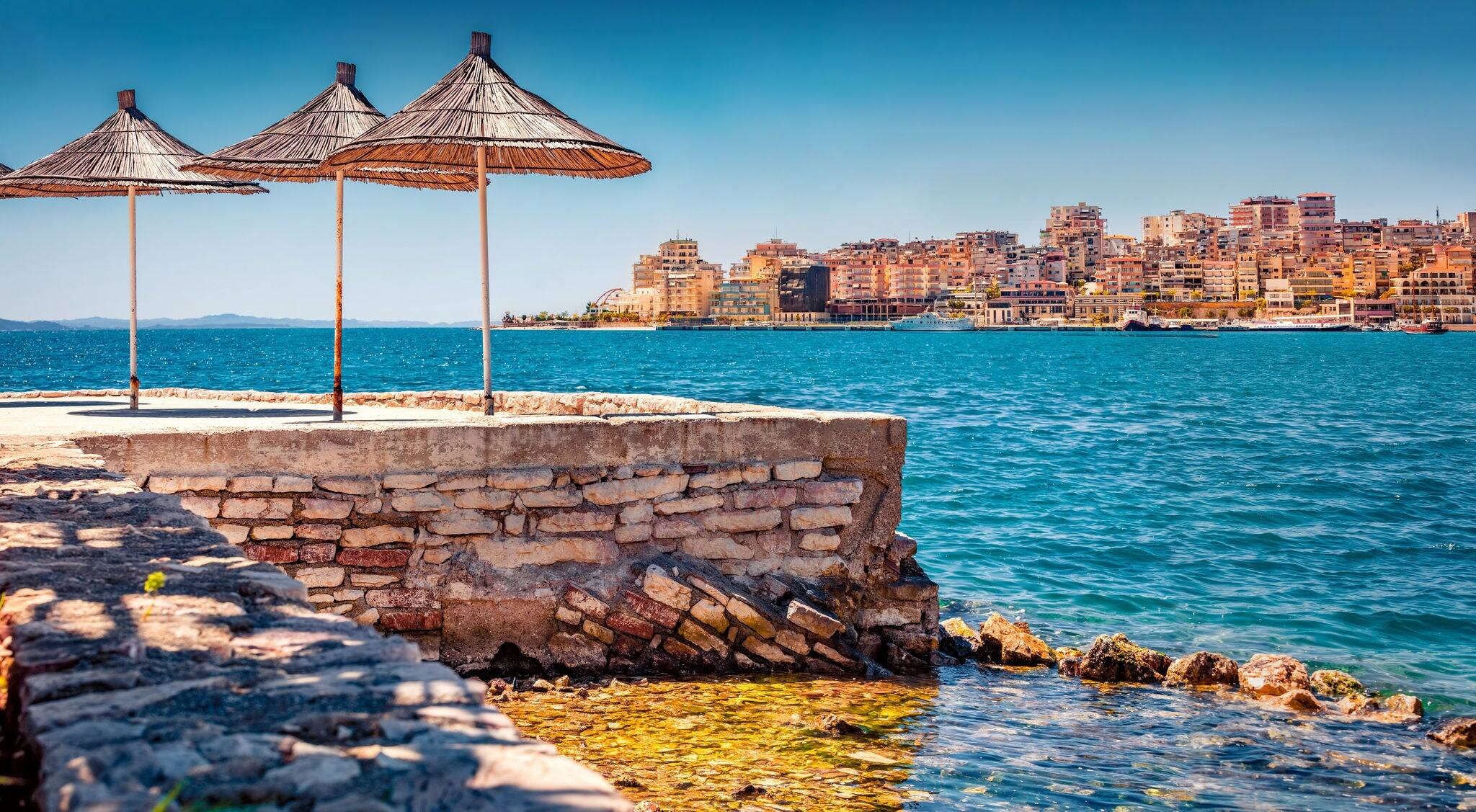 Charming spring cityscape of Saranda tiwn. Marvelous summer view of Albanian Riviera, in southern Albania, Europe. Superb morning scene of Ionian sea with straw umbrellas.