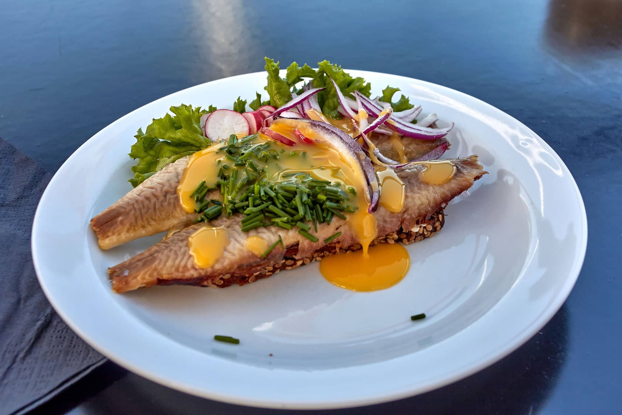 Sol over Gudhjem (Sun over Gudhjem) - traditional Danish sandwich with rugbrod, smoked herring, lettuce, onion, raddish, chives and a raw egg yolk on top, Bornholm island, Denmark.