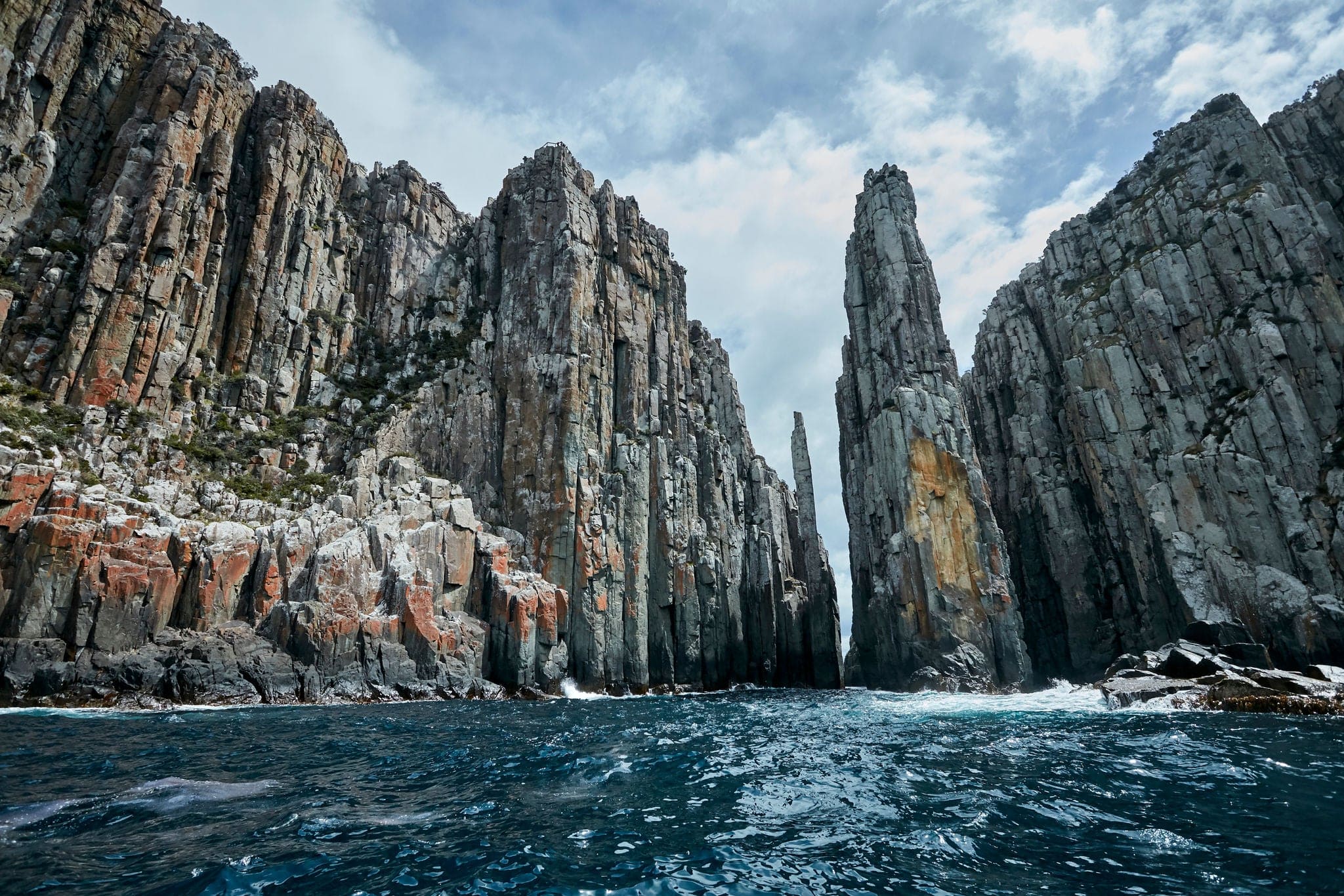 Dolerite cliffs of the Tasman Peninsula as viewed from a boat out at sea.  In the middle are the totem pole and needle, a destination for experienced climbers. Port Arthur, Tasmania, Australia