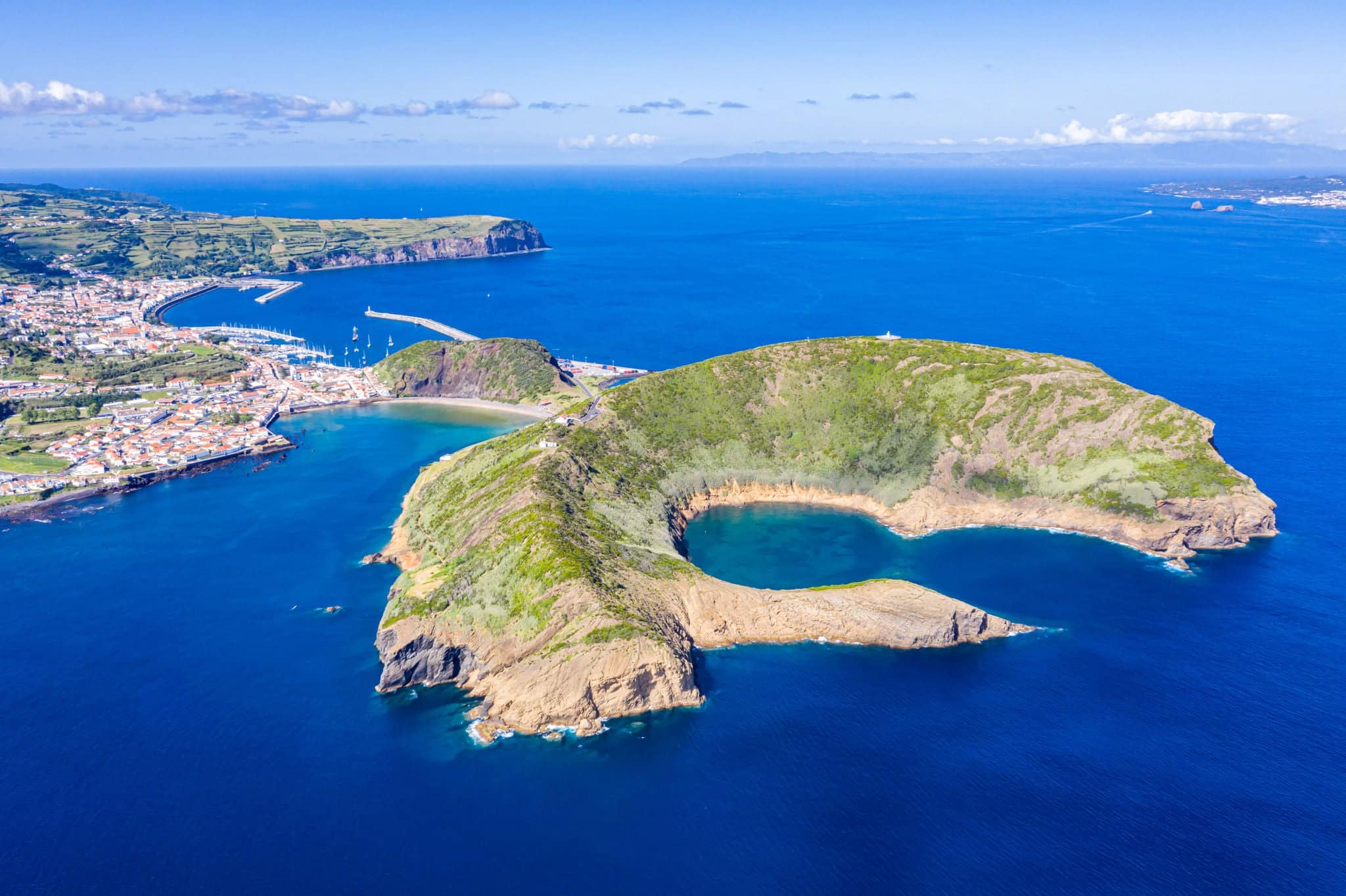 Parque Natural de cráteres volcánicos extintos destruidos de Caldeirinhas, montaña Guia, baia (bay) do Porto Pim y puerto, playas, puertos deportivos, techos rojos de la histórica ciudad de Horta, isla Faial, Portugal.