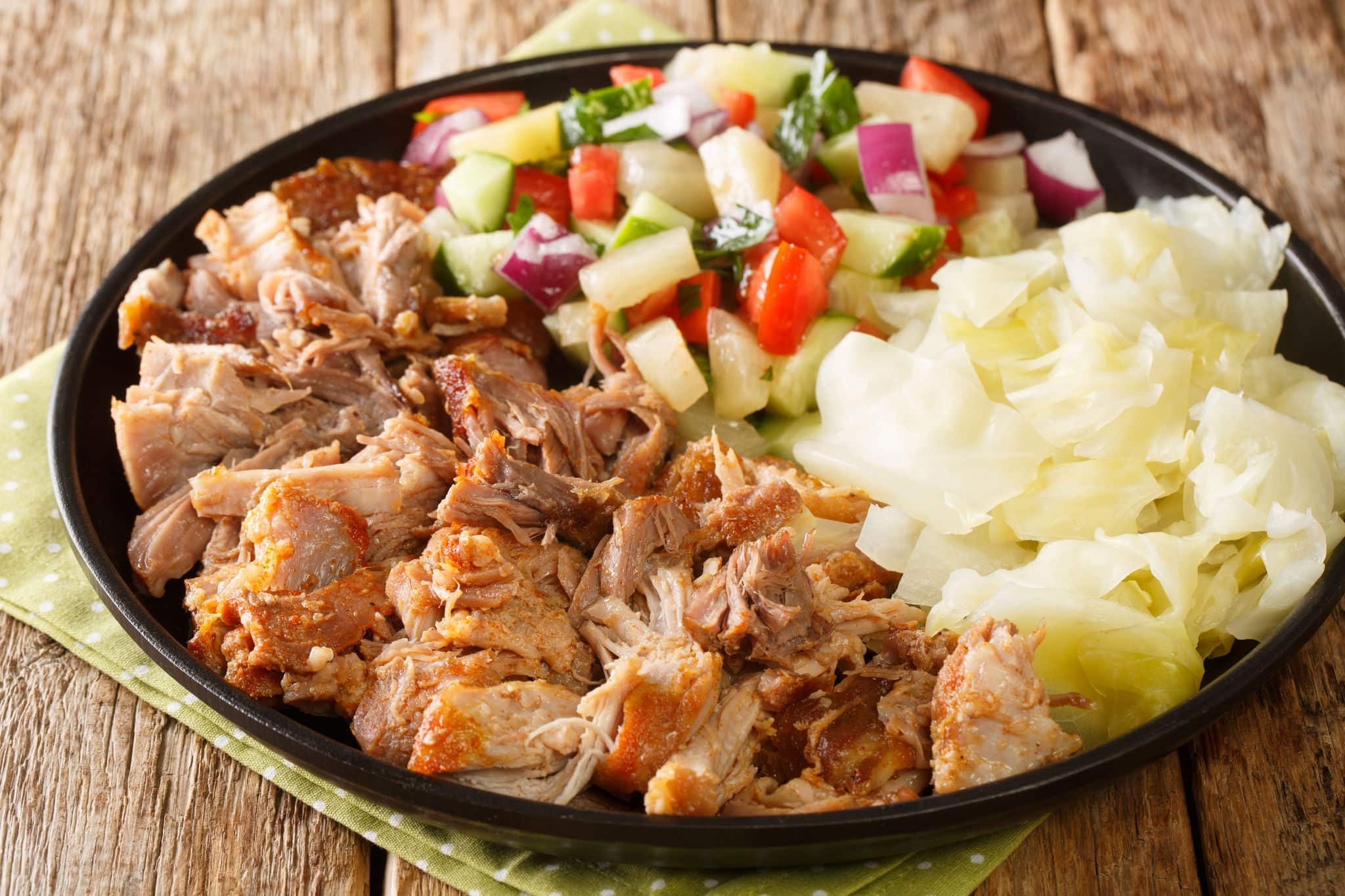 Kalua pork hawaiian food slowly cooked and served with stewed cabbage and fresh salad close-up in a plate on the table. horizontal