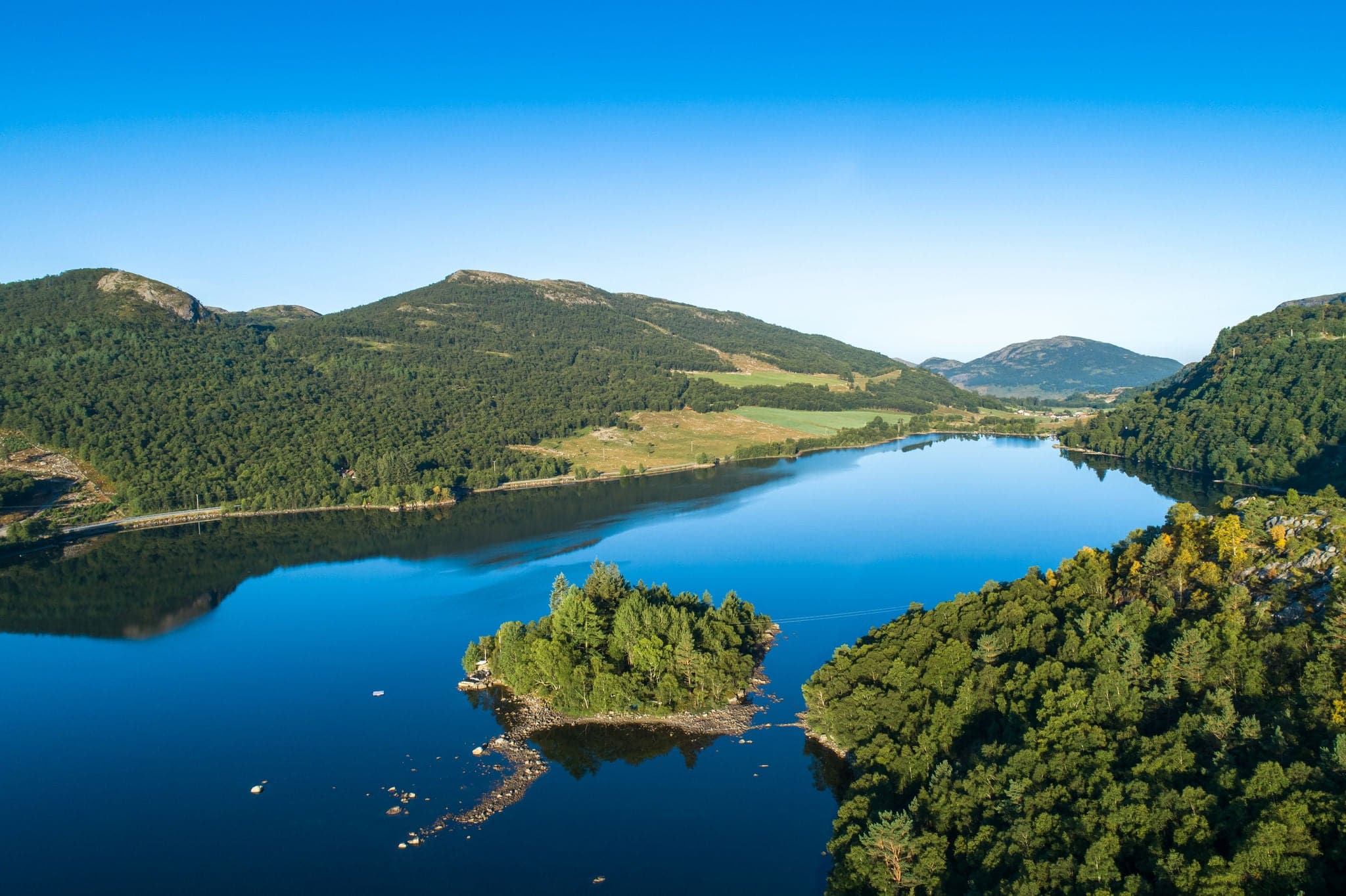 Aerial early summer morning view of lush green valley with lake surrounded by mountain range near Sandnes in Norway