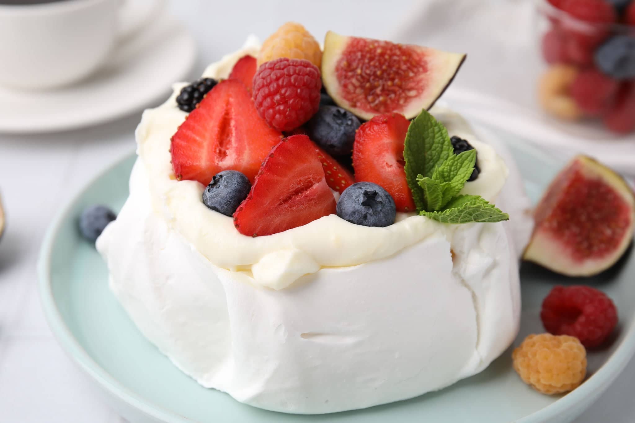 Pavlova cake (meringue dessert) with whipped cream, fresh berries, mint and fig on table, closeup