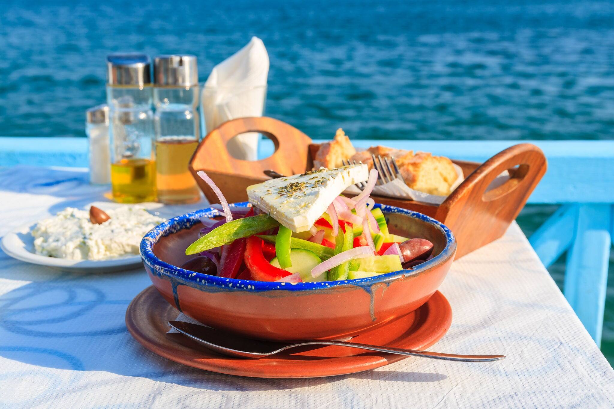 Greek salad on table in Greek tavern with blue sea water in background, Samos island, Greece
