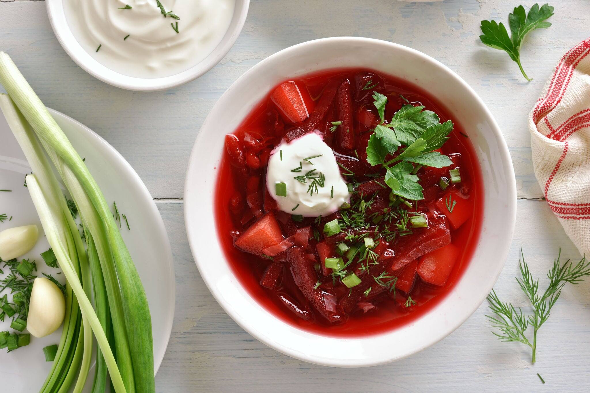 Tasty beetroot soup in bowl on white wooden background. Traditional ukrainian russian soup (borscht) with greens and sour cream. Top view, flat lay