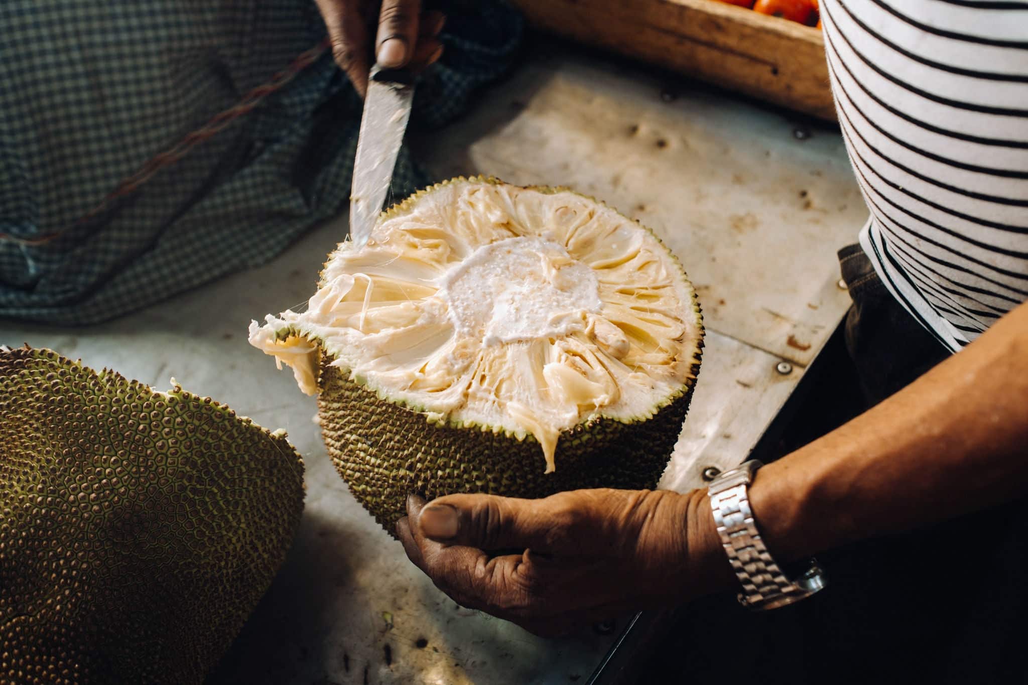 The seller cuts a juicy, ripe jackfruit for tourists. The urban market of Port Louis, Mauritius.