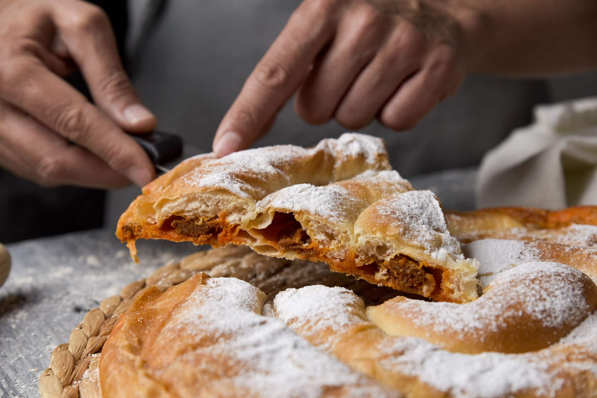 closeup of a young caucasian man serving a piece of on an ensaimada, a pastry typical of Mallorca, Spain, filled with sobrasada, placed on a rustic wooden table