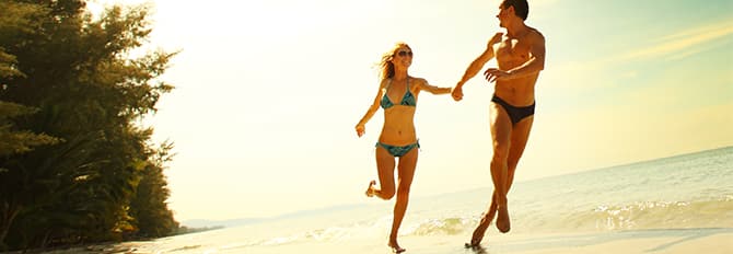 Una pareja corriendo por la playa mientras disfruta del sol y la brisa fresca